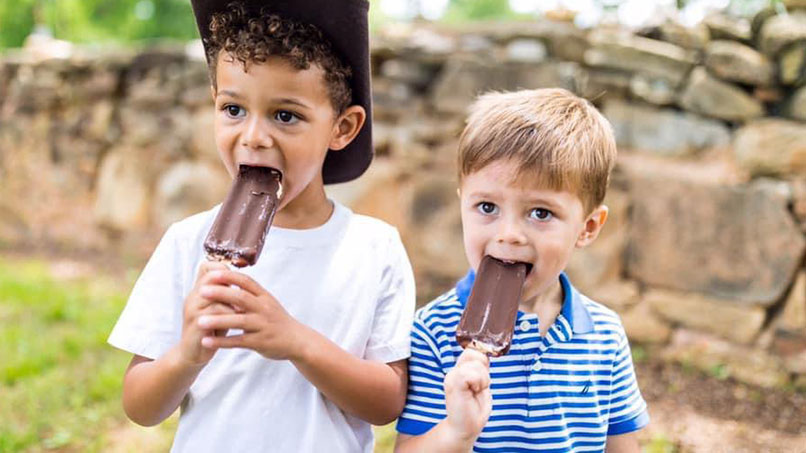 SMED_ContentContributors_IceCream_BigSandyCreek_3_806x453px.jpg Two children enjoying chocolate-covered ice cream bars outdoors during a summer gathering.