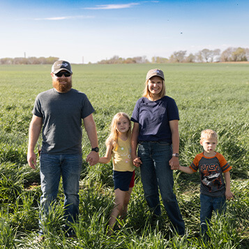 IMG_1971.jpg Farmers pose with their children in a field of grass.