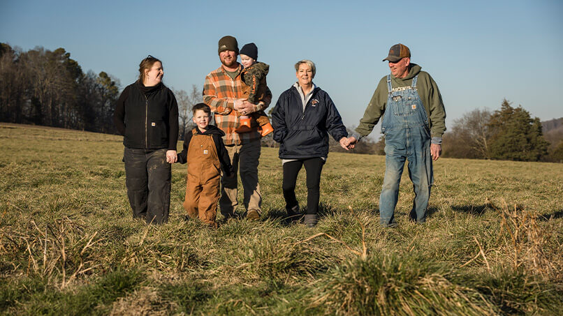 250111-Barham-Jersey-Farm-056.jpg The Barham Jersey Farm family holds hands while posing for a photo in a field of grass.